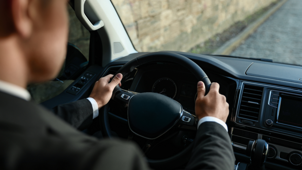 Chauffeur privé en costume noir conduisant un véhicule haut de gamme. Service de transport premium, sécurisé et professionnel à Marseille avec AMAN Chauffeur.