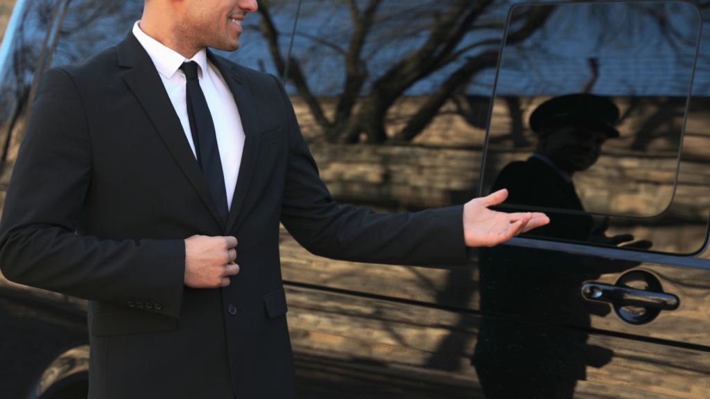 Chauffeur privé en costume noir accueillant un client devant un véhicule haut de gamme. Service de transport premium à Marseille avec AMAN Chauffeur.