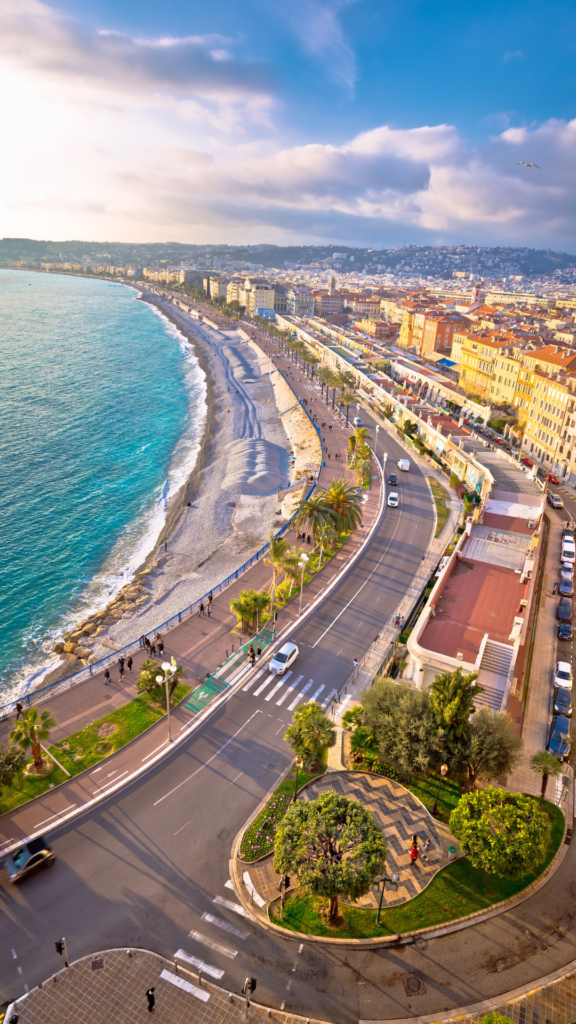 Vue panoramique sur la Promenade des Anglais à Nice, longeant la Méditerranée sous une lumière dorée.